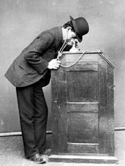 La version de 1895 du kinétophone en usage, montrant le casque qui mène le cylindre phonographique au cabinet